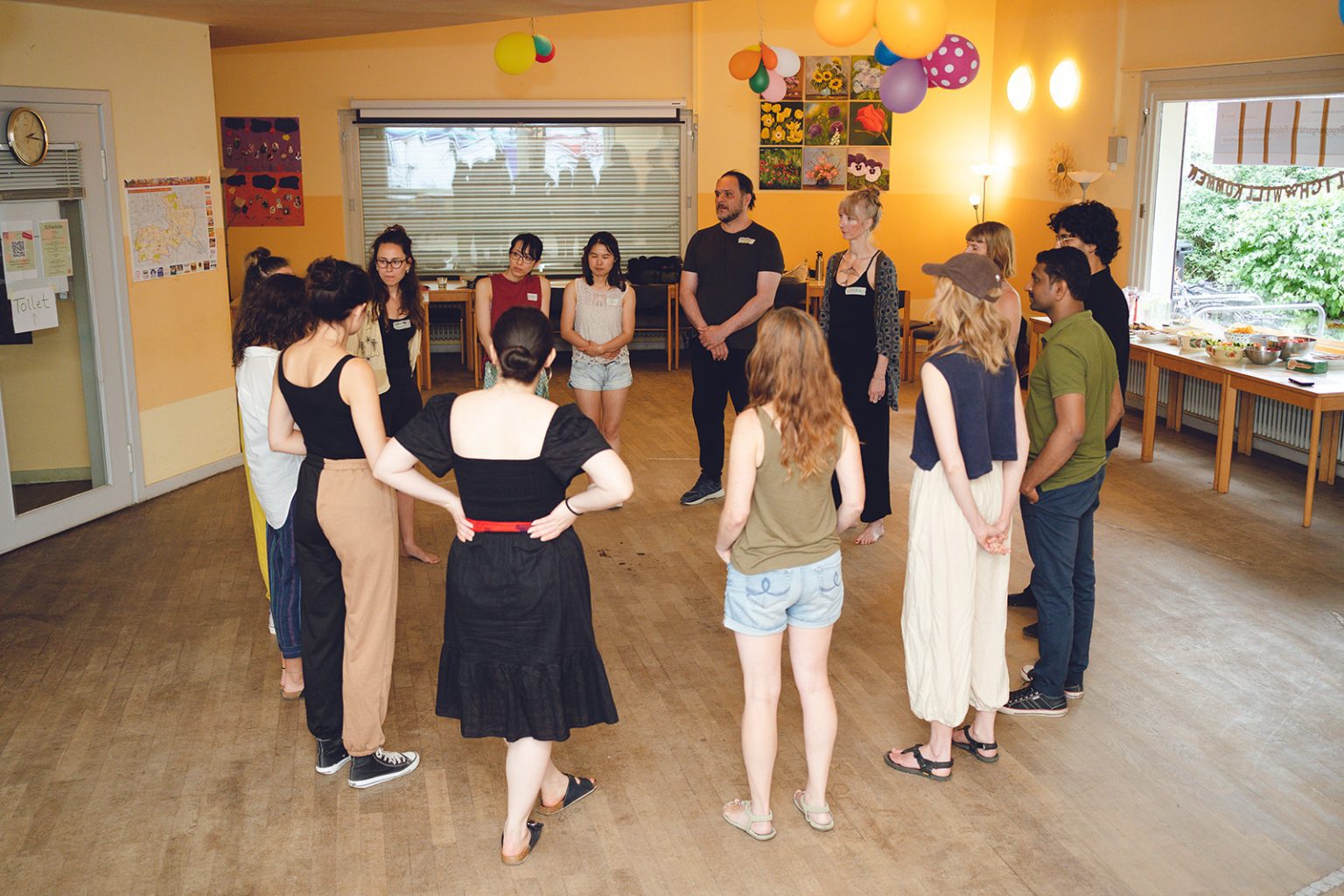 Here you see a picture of a workshop where people are standing in a circle listening to one person explaining an activity. This picture is use for the contact page